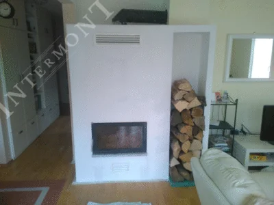 Obloge kamina - Intermont Završeni moderni kamin u bijeloj oblozi u dnevnom boravku s parketom. Kamin ima ugrađeno ložište sa staklom, gornju ventilacijsku rešetku za topli zrak, donji otvor, te nišu za skladištenje drva s desne strane.